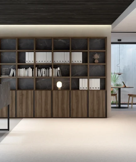 Oficina a medida con librería grande, mesa de trabajo en acabado negro y zona de reunión con mesa redonda y muebles bajos de almacenamiento.